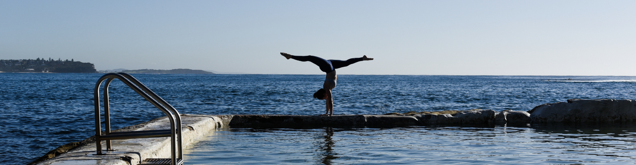 Kat Clayton doing a yoga Handstand over the calm ocean